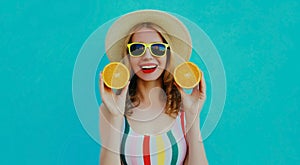 Summer portrait happy smiling woman holding in her hands two slices of orange fruit in straw hat on a colorful blue background