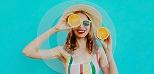 Summer portrait happy smiling woman holding in her hands two slices of orange fruit in straw hat on a colorful blue background