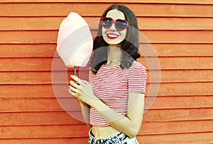 Summer portrait of happy smiling young woman with cotton candy in amusement park on wooden wall