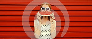 Summer portrait of happy smiling young woman eating fresh juicy fruits, slice of watermelon wearing heart shaped sunglasses on red