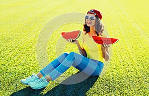 Summer portrait of happy smiling young woman eating fresh juicy slice of watermelon on the grass in the summer park