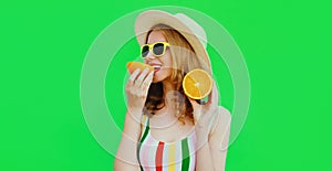 Summer portrait happy smiling young woman eating slices of orange wearing a straw hat, sunglasses on green background