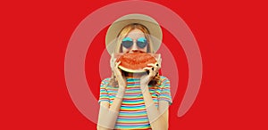 Summer portrait of happy smiling young woman with fresh juicy slice of watermelon wearing straw hat on red studio background