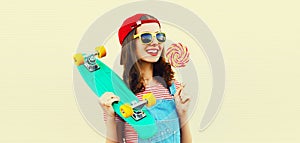 Summer portrait of happy smiling young woman with lollipop and green skateboard wearing baseball cap on white background