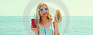 Summer portrait of happy smiling young woman with papaya and cup of juice on the beach on sea background