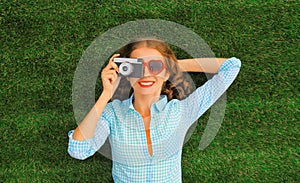 Summer portrait of happy smiling young woman photographer taking pictures on camera lying on the grass in the park