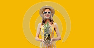 Summer portrait of happy smiling young woman with pineapple fruit on yellow studio background