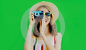 Summer portrait happy smiling young woman with retro camera wearing a straw hat on green background