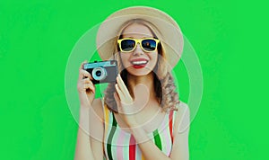 Summer portrait happy smiling young woman with retro camera wearing a straw hat on green background