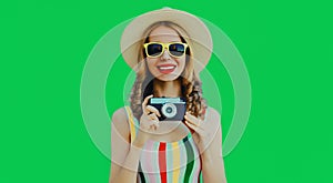 Summer portrait happy smiling young woman with retro camera wearing a straw hat on green background