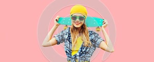 Summer portrait of happy smiling young woman with skateboard wearing colorful clothes on pink background