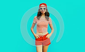 Summer portrait happy smiling young woman wearing baseball cap, red shorts on blue background