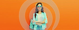 Summer portrait of happy smiling young woman wearing straw hat, backpack and shirt on orange background, blank copy space for