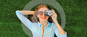 Summer portrait of happy woman taking pictures on camera lying on green grass in the park