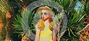Summer portrait of happy young woman drinking fresh juice with pineapple wearing straw hat on the beach with palm tree background