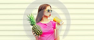 Summer portrait of happy young woman drinking fresh juice with pineapple wearing sunglasses on white background