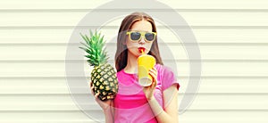 Summer portrait of happy young woman drinking fresh juice with pineapple wearing sunglasses on white background