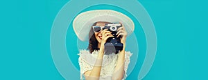 Summer portrait of happy young woman photographer with film camera wearing white straw hat on blue background