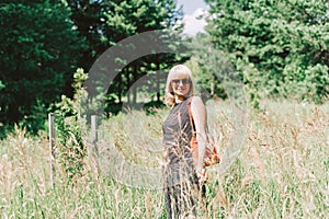 Summer portrait of mature adult blonde woman sitting in a grass on sunny day in the meadow