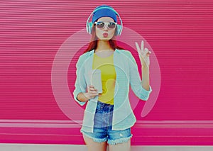 Summer portrait of modern young woman listening to music in headphones on pink background