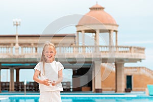 Summer. Portrait of a small Caucasian girl laughing merrily. Outdoor. In the background is a complex with a swimming pool. The