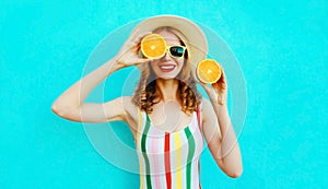 Summer portrait smiling woman holding in her hands two slices of orange fruit hiding her eye in straw hat on colorful blue