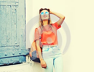 Summer portrait of stylish blonde young woman wearing backpack, sunglasses in the city