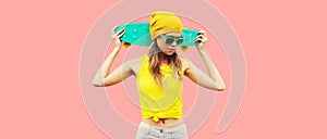 Summer portrait of stylish cool young woman with skateboard wearing colorful clothes on pink background