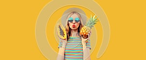 Summer portrait of stylish young woman with fresh juicy fruits pineapple and papaya blowing her lips sending air kiss wearing