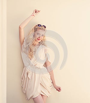 Summer portrait of young beautiful blond woman in white dress posing near the wall and have fun. Toned in warm colors