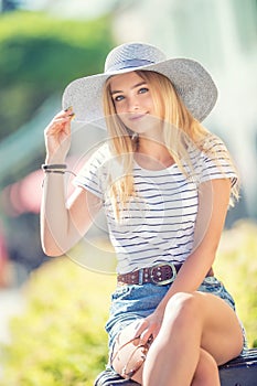 Summer portrait of young beautiful woman in hat sitting on bench in park