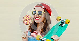 Summer portrait of young smiling woman with lollipop and green skateboard wearing a baseball cap on white background