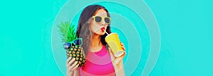 Summer portrait of young woman drinking juice and holding pineapple wearing sunglasses on blue background