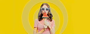 Summer portrait of young woman with juicy lollipop or ice cream shaped slice of watermelon wearing sunglasses on yellow background