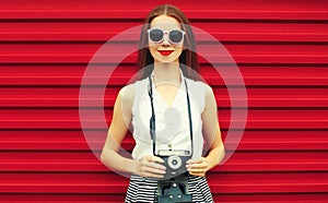 Summer portrait of young woman photographer with vintage film camera on colorful red background