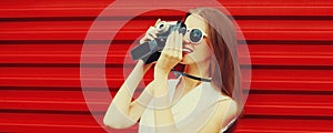 Summer portrait of young woman photographer with vintage film camera on colorful red background