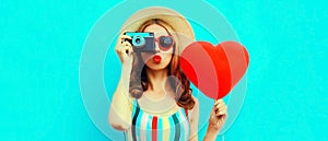 Summer portrait of young woman taking picture on retro film camera with big red heart shaped balloon wearing straw hat on blue