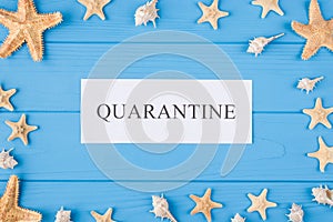 Summer in quarantine concept. Top above overhead view photo of quarantine word and seashells and seafish isolated on blue wooden