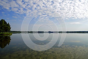 A summer quiet day on a forest lake. Clouds are reflected on the water surface