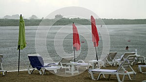 Summer rain, thunderstorm, heavy rainfall on an empty beach, by river. lonely empty sun loungers and beach umbrellas are