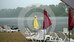 summer rain, thunderstorm, heavy rainfall on an empty beach, by river. lonely empty sun loungers and beach umbrellas are