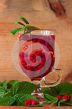 Summer raspberry cold tea in a glass on wooden background. Healthy fruit cocktail. Tasty red juice fresh green leaves