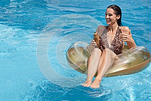 Summer and recreation concept. Attractive woman sitting on big rubber ring in middle of swimming pool, holding cocktail in hand