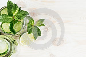 Summer refreshing drink with cucumber, mint, ice and lime on old wood board, top view, border.