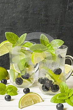 Summer refreshing drinks lemonade or cocktail Mojito with lime fresh mint blueberry ice. Light table, Dark wall