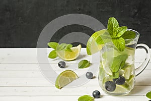 Summer refreshing drinks lemonade or cocktail Mojito with lime fresh mint blueberry ice. Light table, Dark wall