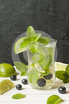 Summer refreshing drinks lemonade or cocktail Mojito with lime fresh mint blueberry ice. Light table, Dark wall