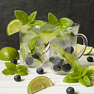 Summer refreshing drinks lemonade or cocktail Mojito with lime fresh mint blueberry ice. Light table, Dark wall