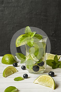 Summer refreshing drinks lemonade or cocktail Mojito with lime fresh mint blueberry ice. Light table, Dark wall