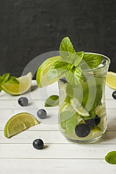 Summer refreshing drinks lemonade or cocktail Mojito with lime fresh mint blueberry ice. Light table, Dark wall